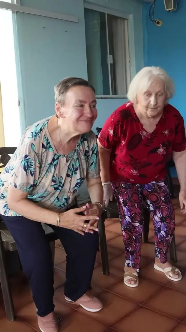 Duas senhoras sorriem sentadas lado a lado