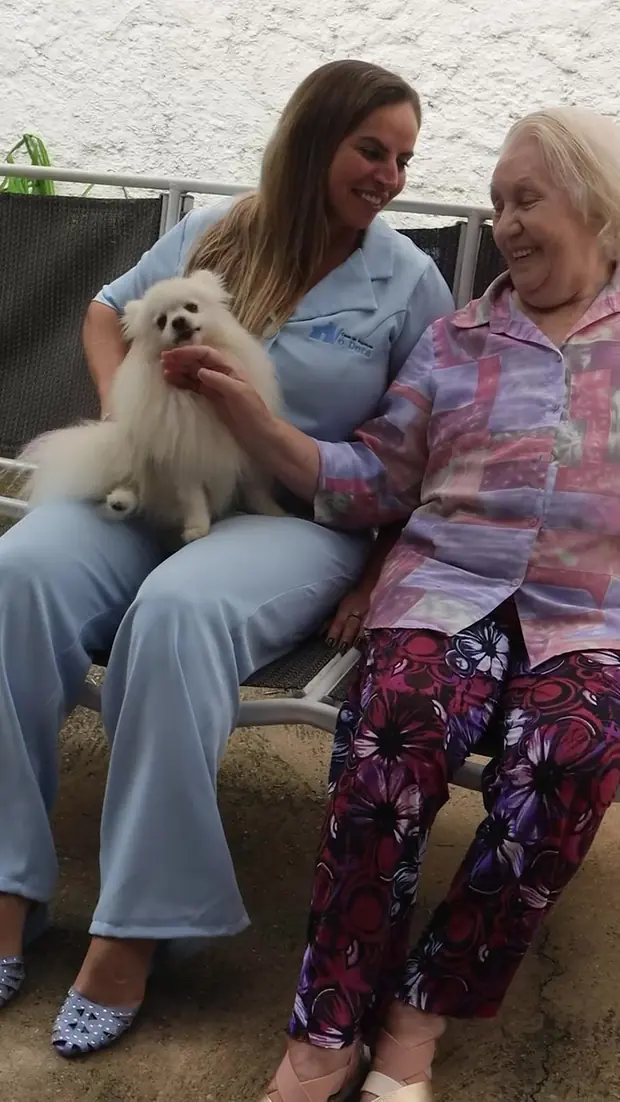 Cuidadora recebe uma senhora na entrada da casa
