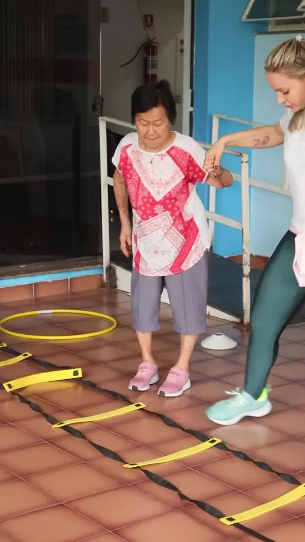 Idosa caminha na escada de agilidade com apoio da fisioterapeuta