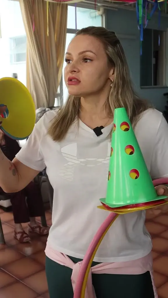 Educadora física explica o exercício segurando um cone de encaixe colorido