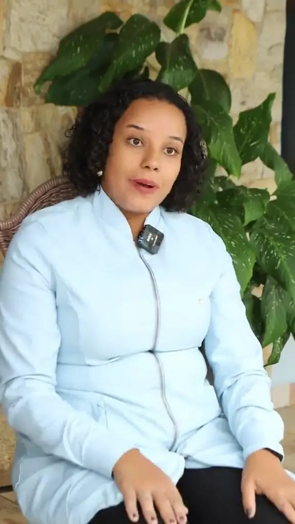 Fisioterapeuta sentada fala para a câmera, com o jardim atrás