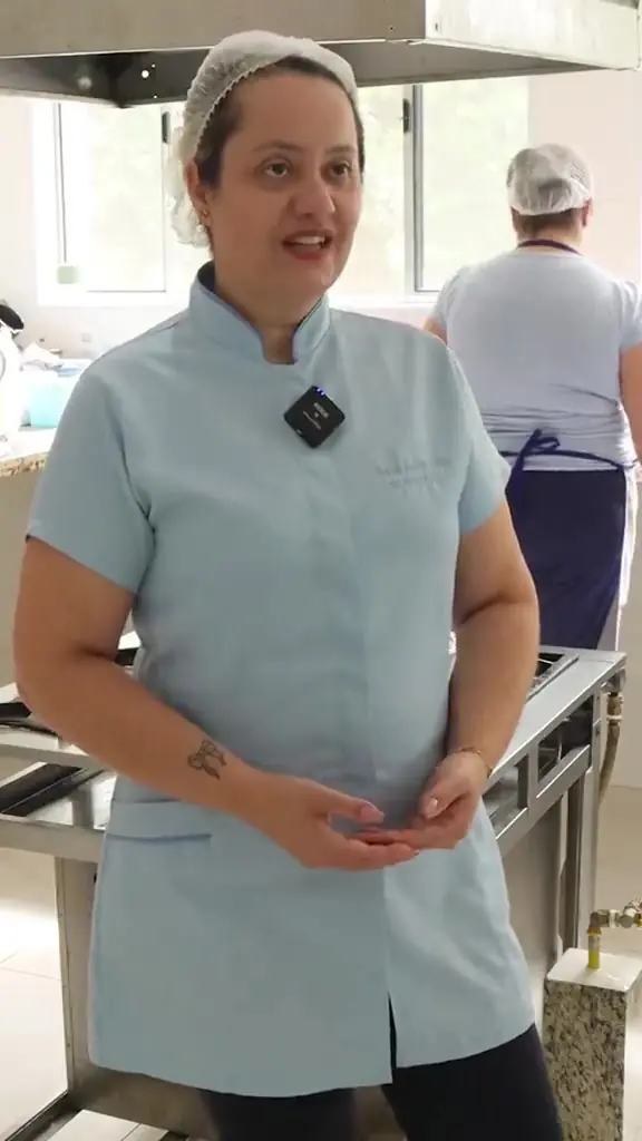 Nutricionista de uniforme fala para a câmera na cozinha da casa