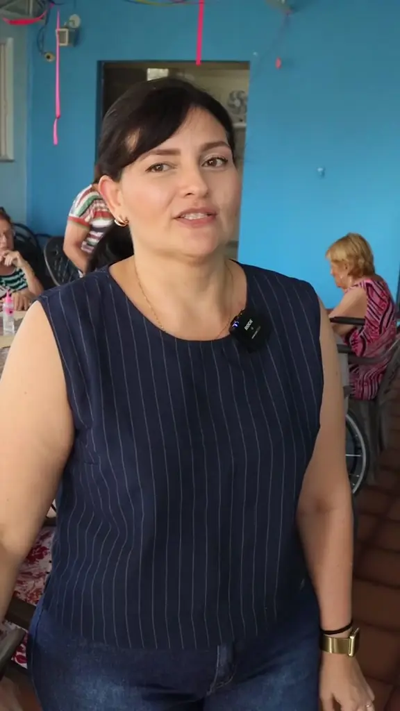 Psicopedagoga fala para a câmera durante a oficina, com o grupo à mesa atrás dela
